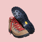 Pair of hiking boots with red laces on a wooden surface and light gray background