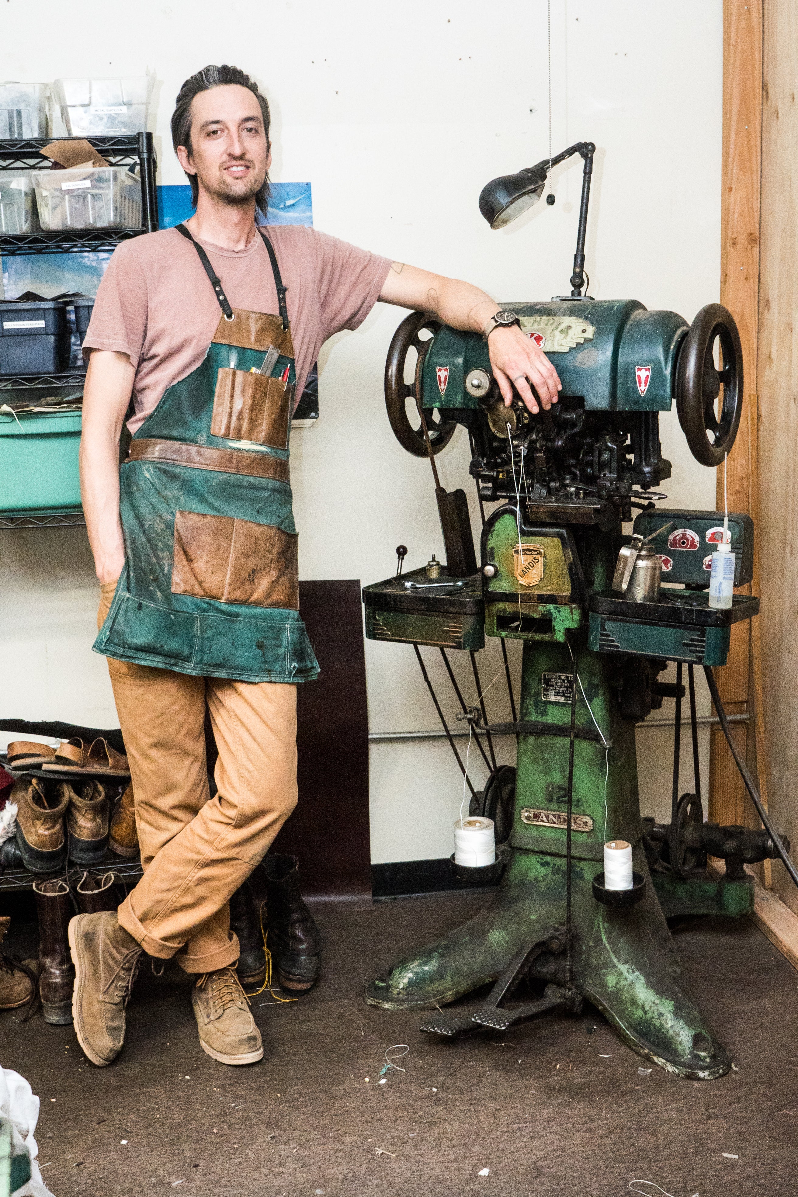 Man in a workshop wearing an apron next to a large green machine.