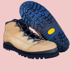 Tan work boots with blue soles on a wooden stool against a white brick wall.