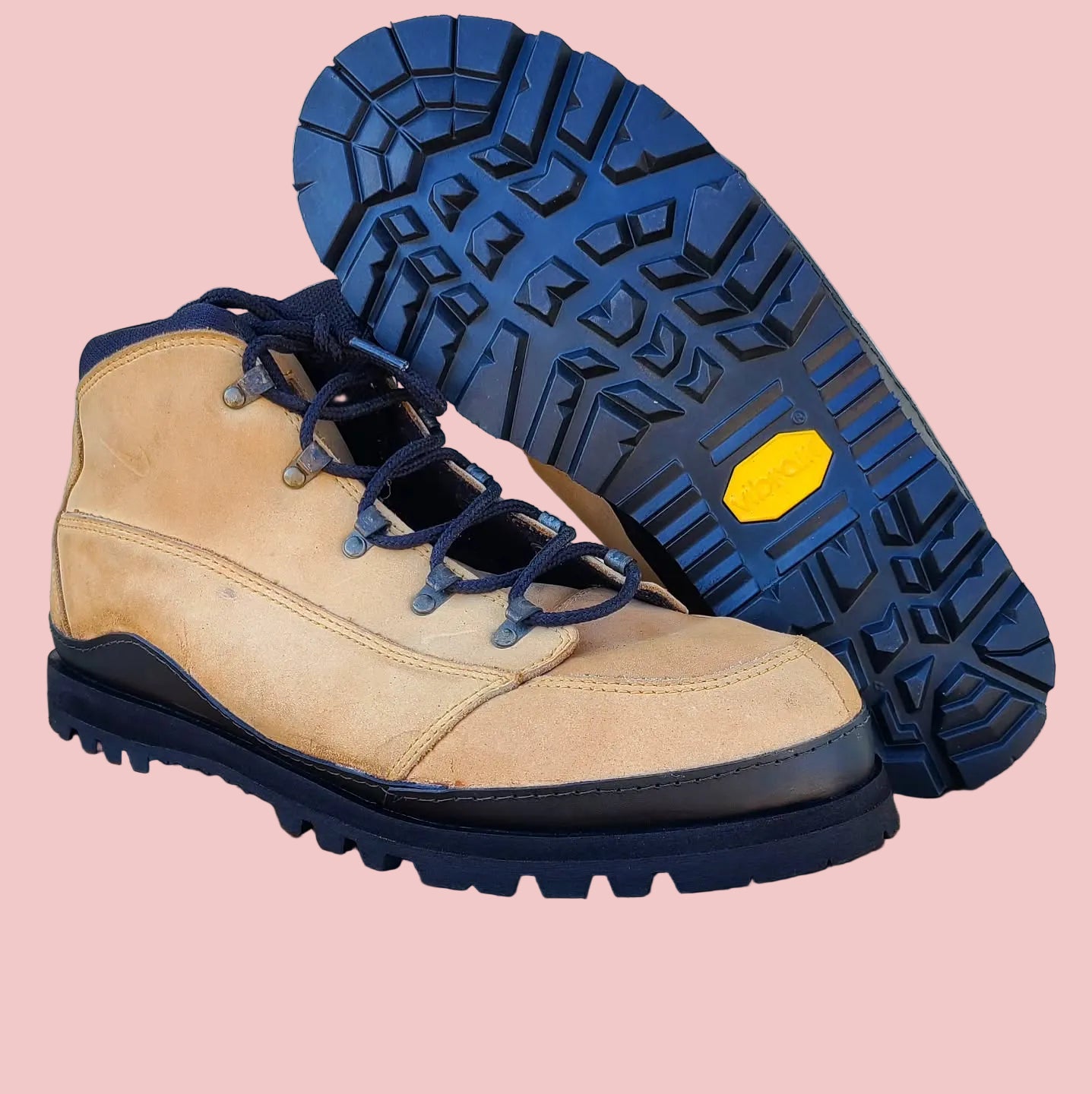 Tan work boots with blue soles on a wooden stool against a white brick wall.