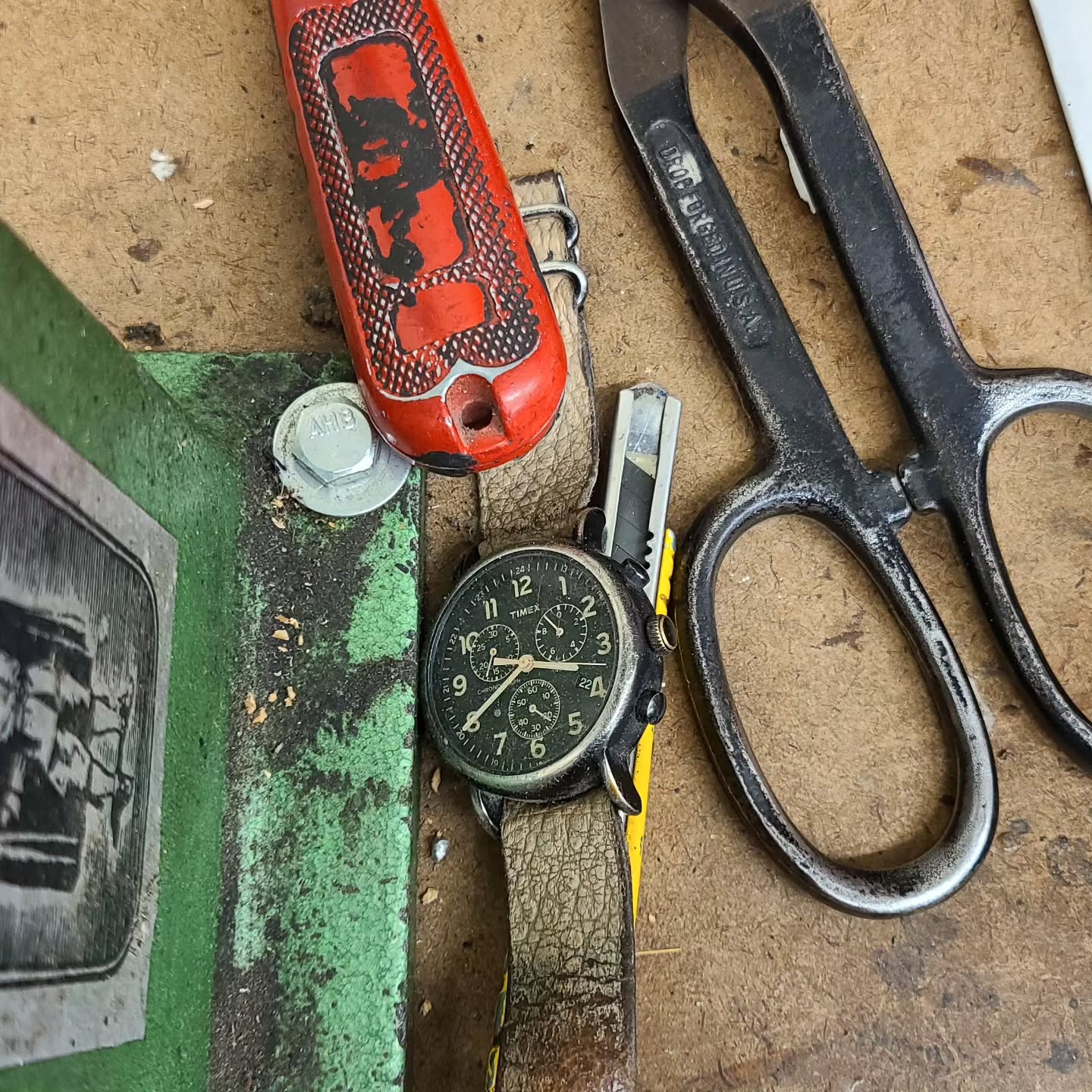 Vintage tools including a pocket knife, scissors, and a watch on a textured surface.